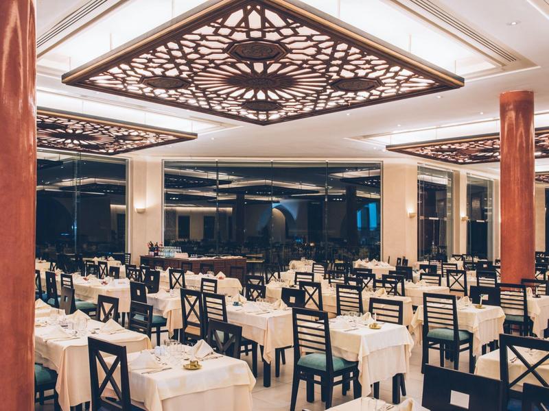 Eleganter Hotelrestaurant mit gedeckten Tischen, dunklen Stühlen und dekorativer Deckenbeleuchtung.