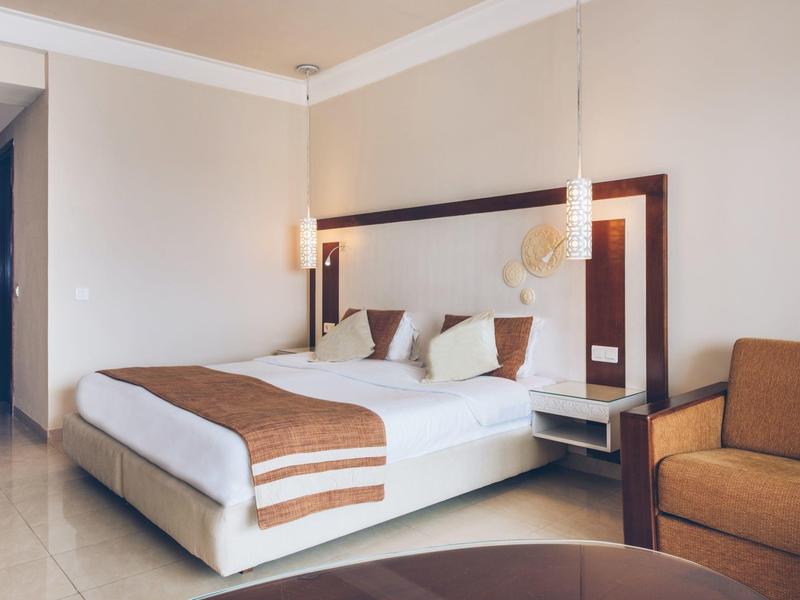 Modernes Hotelzimmer mit großem Bett, zwei Nachtlampen und braunem Sessel.