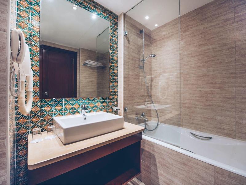 Modernes Hotelbadezimmer mit Waschbecken, großem Spiegel und Badewanne mit Glasabtrennung.