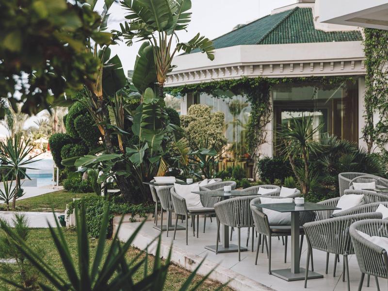 Moderne Außenterrasse mit grauen Stühlen und Tischen, umgeben von üppigem Grün und Pflanzen.