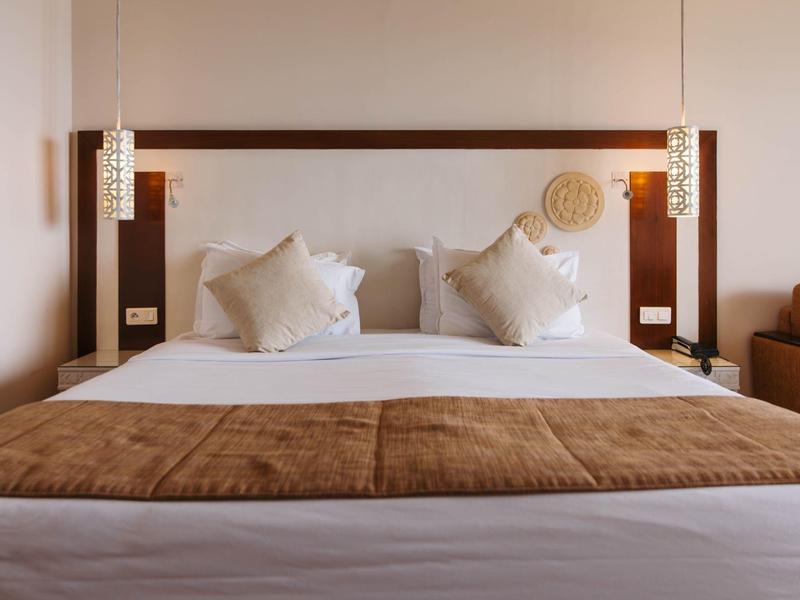 Modernes Hotelzimmer mit großem Bett, weißen Kissen und brauner Bettdecke.