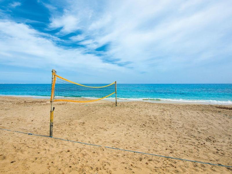 Leerer Volleyballplatz am Sandstrand mit blauem Himmel und Meer im Hintergrund.