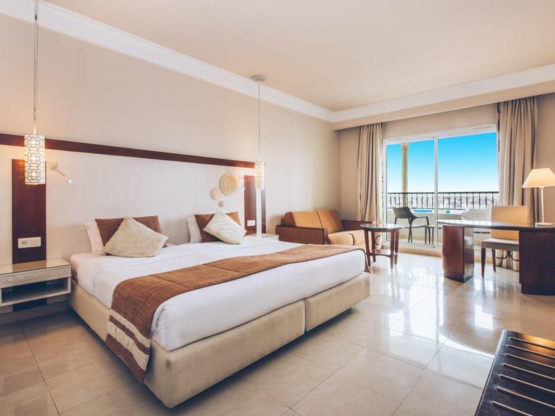 Helles Hotelzimmer mit Doppelbett, Sofa, Arbeitstisch und Balkon mit Meerblick.