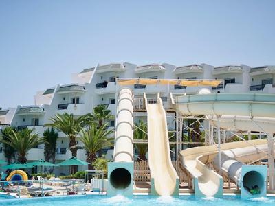 Water park with slides and pool in front of a hotel building under a blue sky.