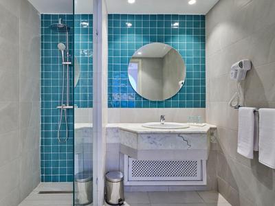 Modernes Badezimmer mit Duschkabine, rundem Spiegel und Waschbecken vor blauen Kacheln.