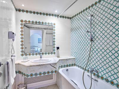 Helles Badezimmer mit Badewanne, Doppelwaschbecken und grün-weißem Fliesenmuster.