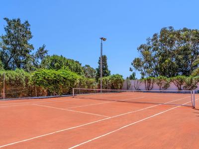 Outdoor red tennis court surrounded by blue sky and green trees.