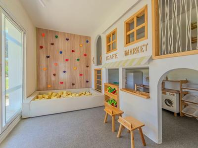 Children's playroom with climbing wall, seating area, and playful kitchen in neutral tones.