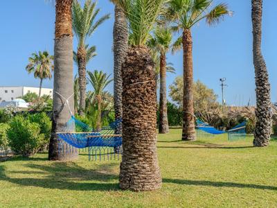Green garden with palm trees and blue hammocks in a hotel area.