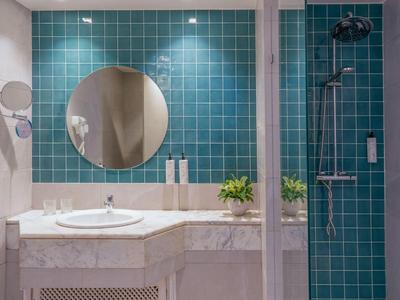 Bathroom with round mirror, sink, green tiled wall, and shower area.