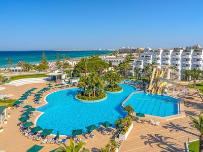 Large pool with island, sunbeds, and palm trees next to a hotel by the sea.