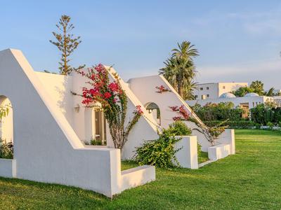White hotel buildings with architectural arches and blooming bougainvillea in a green garden.