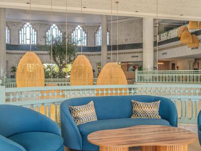 Modern hotel lounge area with blue chairs, wooden tables, and large hanging lamps.