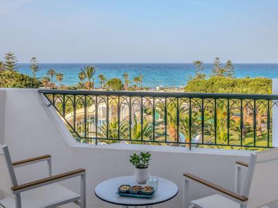 Balcony with table and chairs overlooking palm trees and the sea in the background.