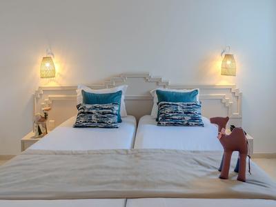 Two single beds with blue pillows, nightstands, and lamps in a simple white hotel room.