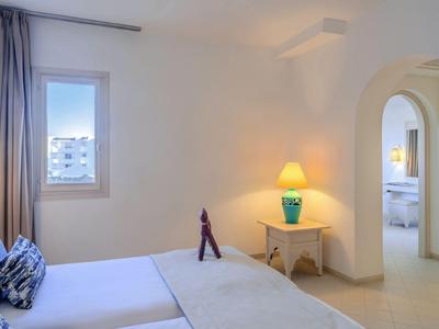 Brightly decorated hotel room with double bed, bedside lamp, and view through an archway to a bathroom.