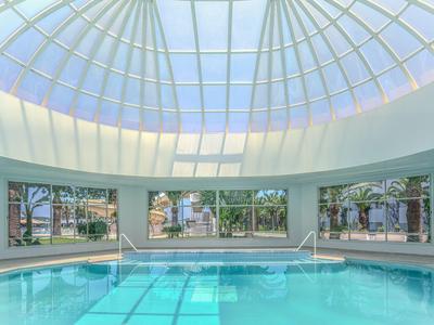 Indoor swimming pool under a large glass dome with views of palm trees and outdoor areas.
