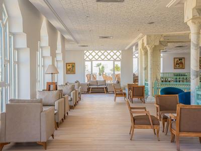 Bright hotel lounge area with comfortable armchairs and wooden tables near large windows.