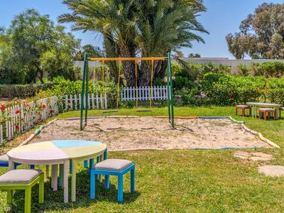 Children's playground with sandbox, swing, and colorful tables in a hotel garden.