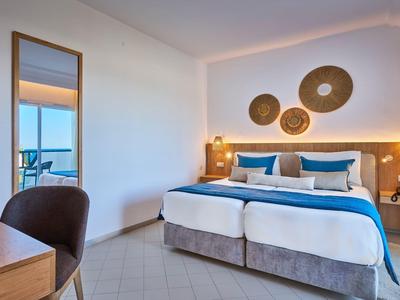Modern hotel room with double bed, blue accents, and view of balcony and sea.