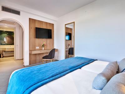 Modern hotel room with double bed, blue bedspread, and wall-mounted TV.