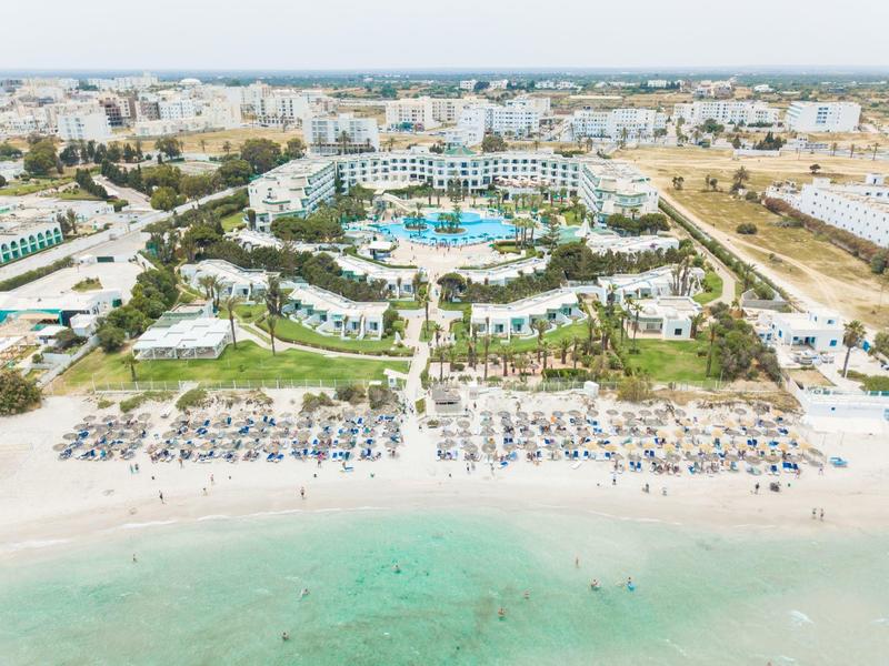 Large beach hotel with pool and numerous sun loungers directly on the turquoise sea.