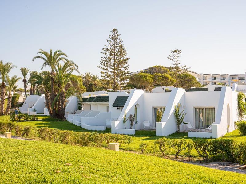 White bungalows in a sunny green hotel area with palm trees.