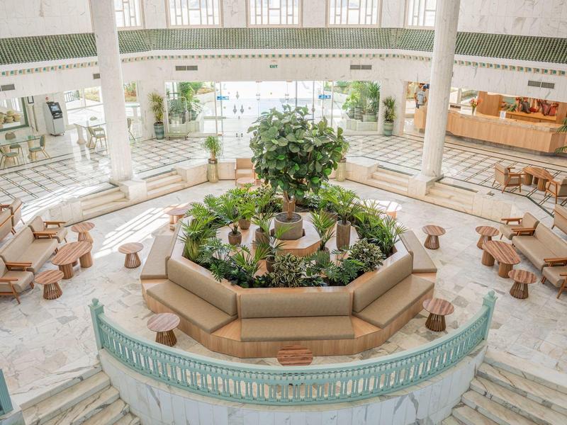 Spacious hotel lobby with central indoor plant arrangement and seating areas.