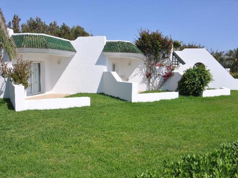 White modern bungalows with green roofs on lush green lawn under clear blue sky.