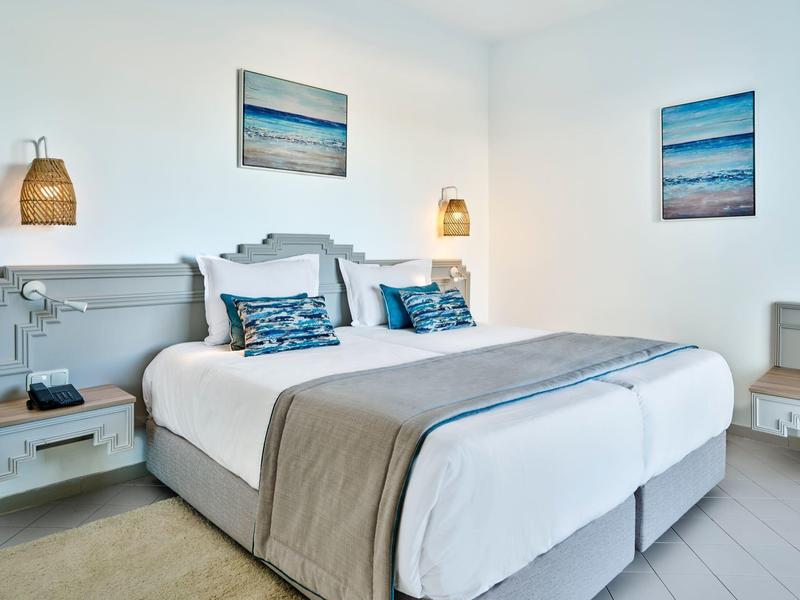 Modern hotel room with two single beds, gray furniture, and maritime wall art.
