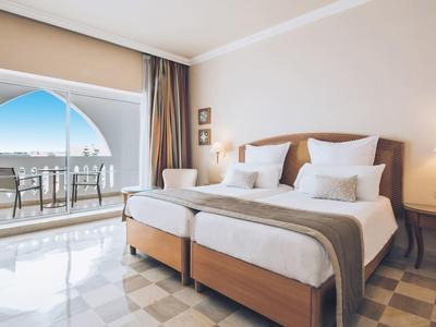 Bright hotel room with two single beds and balcony overlooking the sea.