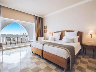 Bright hotel room with two single beds and balcony with sea view.