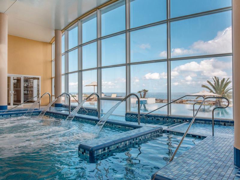 Indoor pool with large windows overlooking palm trees and sky