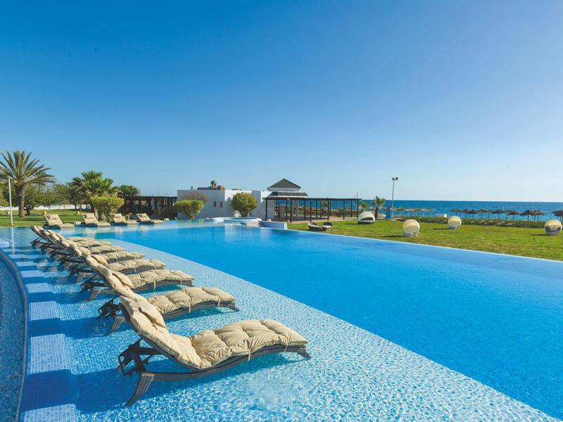 Large outdoor pool with lounge chairs and sea view on a sunny day.