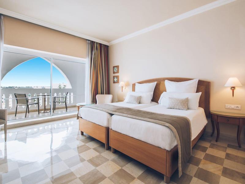 Bright hotel room with two single beds and balcony with sea view.