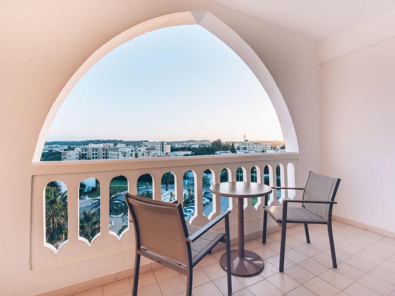 Balcony with arched opening overlooking city and hills, table and two chairs present