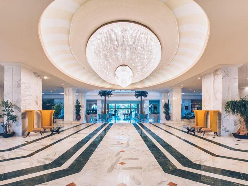 Spacious hotel lobby with marble flooring, chandelier, and seating areas.