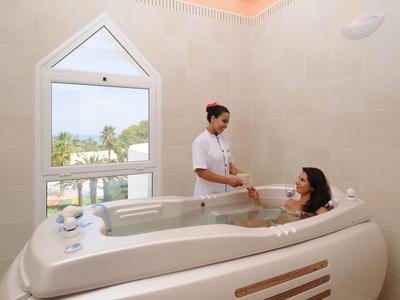 Eine Frau erhält in einem modernen, weißen Wellnessbad eine entspannende Massage im großen Whirlpool.