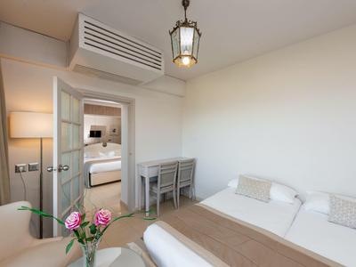 Helles Hotelzimmer mit Bett, Schreibtisch, Sessel und Blick ins Badezimmer.