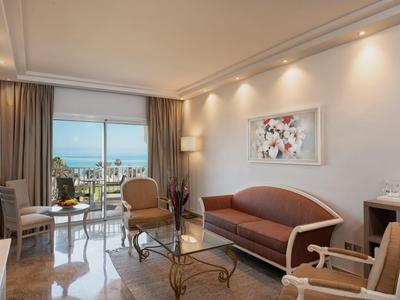 Modern eingerichtetes Hotelzimmer mit Meerblick, Sofa, Sesseln und einem Tisch.