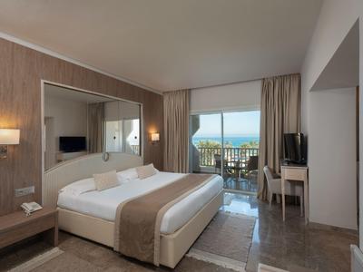 Modernes Hotelzimmer mit Doppelbett, Schreibtisch, TV und Balkon mit Meerblick.