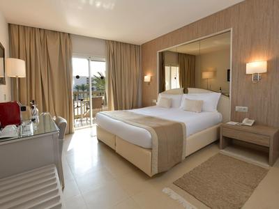 Helles Hotelzimmer mit Doppelbett, Schreibtisch, Balkon und moderner Einrichtung.