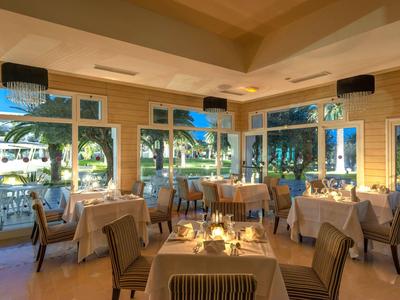 Elegantes Restaurant mit gedeckten Tischen, Kerzenlicht und großen Fenstern mit Blick auf Palmen.