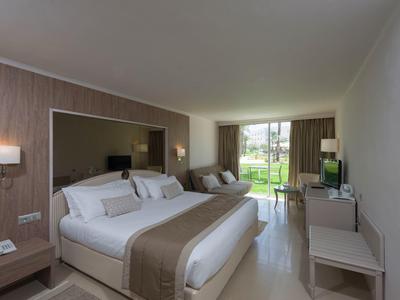 Modern eingerichtetes Hotelzimmer mit großem Doppelbett und Blick auf eine Terrasse.