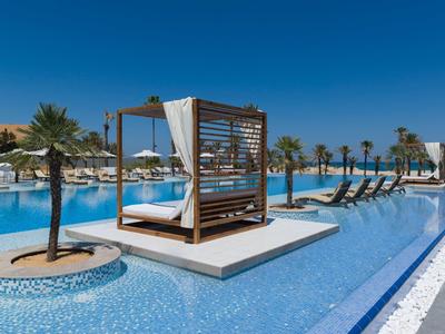 Moderner Pool mit Liegen, Palmen und Baldachin unter klarem, blauem Himmel an sonnigem Tag.