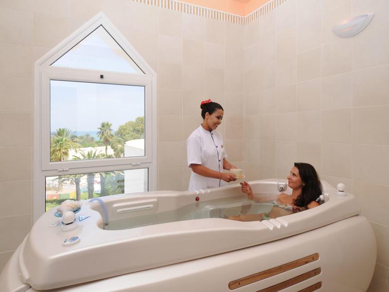 Eine Frau erhält in einem modernen, weißen Wellnessbad eine entspannende Massage im großen Whirlpool.