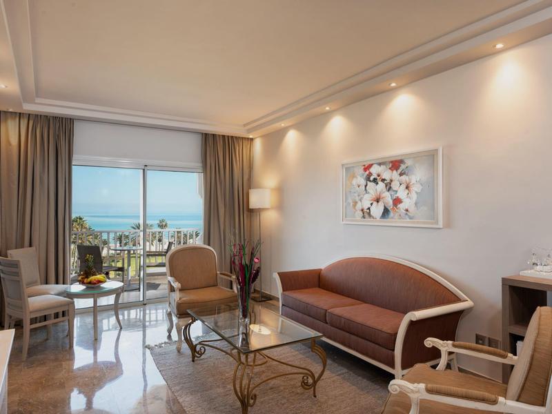 Modern eingerichtetes Hotelzimmer mit Meerblick, Sofa, Sesseln und einem Tisch.