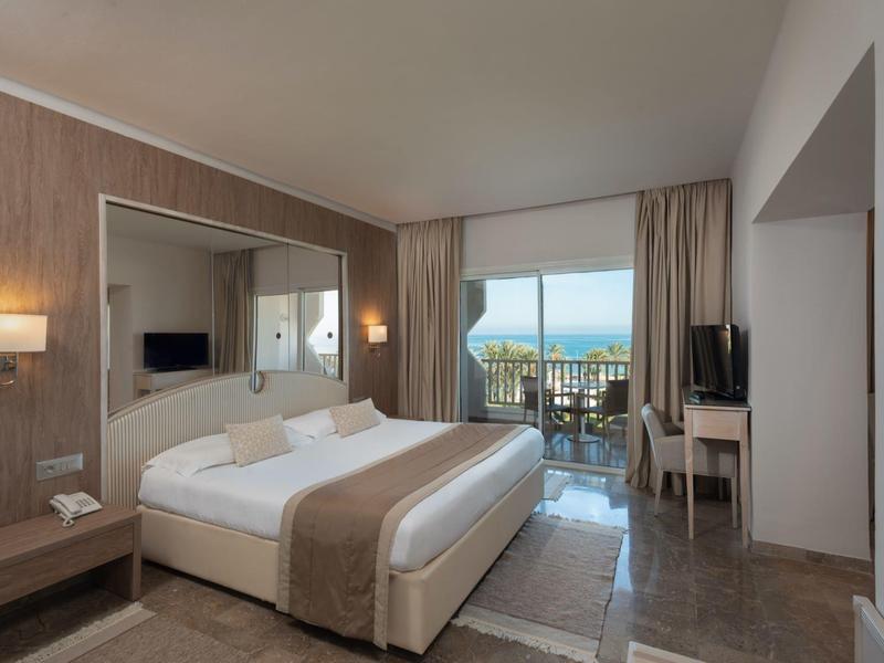 Modernes Hotelzimmer mit Doppelbett, Schreibtisch, TV und Balkon mit Meerblick.