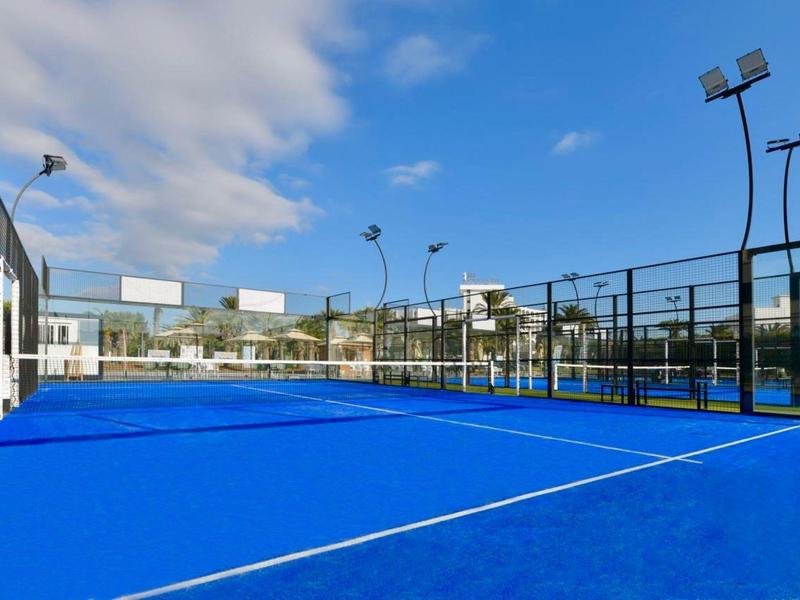 Blauer Paddle-Tennisplatz mit Zäunen und Beleuchtung bei klarem Himmel.