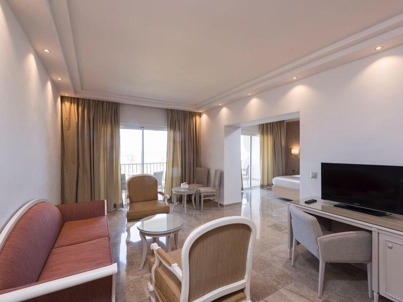 Heller, moderner Wohnraum mit Sofa, Sesseln, Couchtisch und TV in einer Hotelunterkunft.